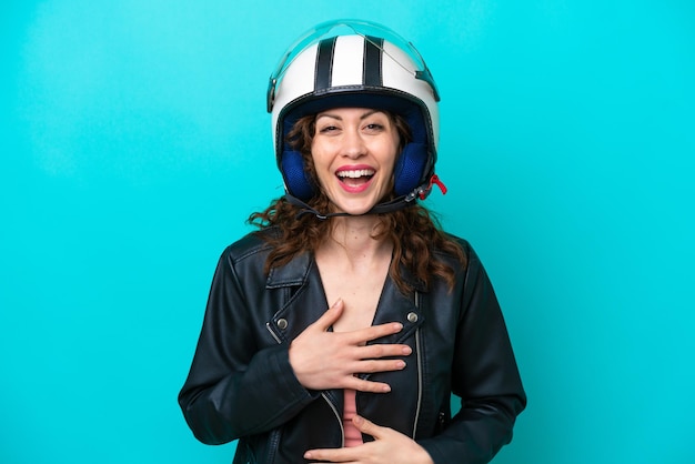 Mujer caucásica joven con un casco de motocicleta aislado sobre fondo azul sonriendo mucho