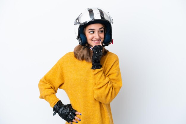 Mujer caucásica joven con un casco de motocicleta aislado sobre fondo blanco pensando en una idea mientras mira hacia arriba