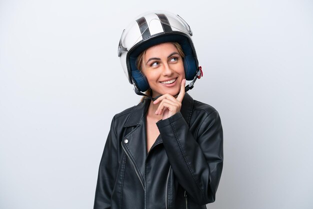 Mujer caucásica joven con un casco de motocicleta aislado sobre fondo blanco pensando en una idea mientras mira hacia arriba