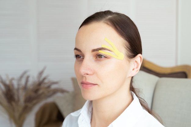 Mujer caucásica joven con cintas de colores en la cara. Cinta estética facial. Concepto de elevación de la piel.