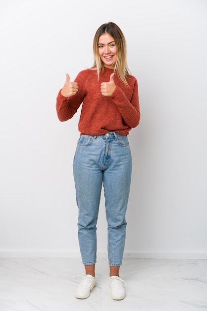 Mujer caucásica joven de cuerpo completo levantando ambos pulgares, sonriente y confiado.