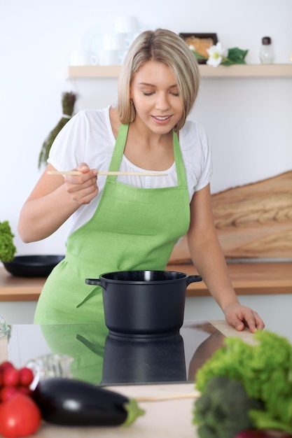 Mujer caucásica joven en un delantal verde que cocina en la cocina