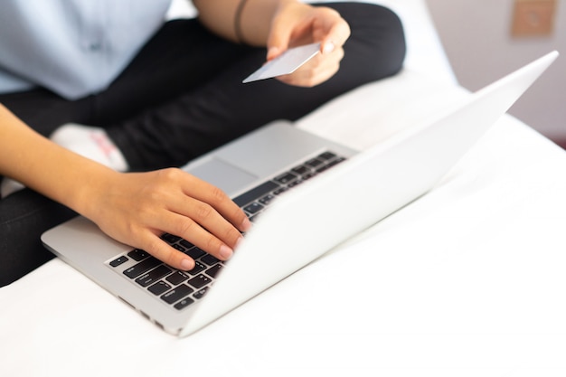 Mujer caucásica joven escribiendo código de acceso en la computadora portátil y con tarjeta de crédito para el pago