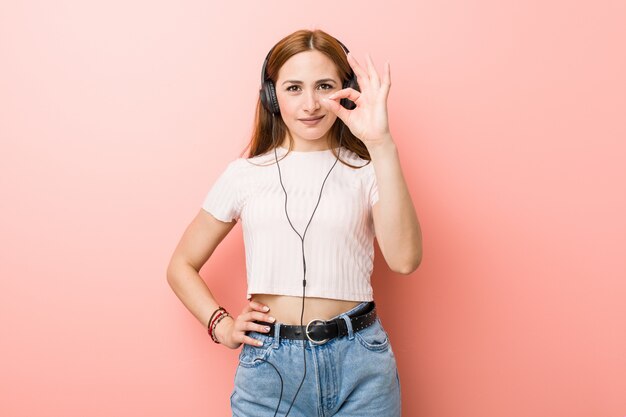 La mujer caucásica joven escucha la música alegre y confiada que muestra gesto aceptable.