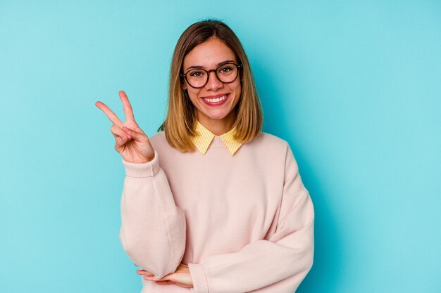 Mujer caucásica joven estudiante aislada en la pared azul que muestra el número dos con los dedos.