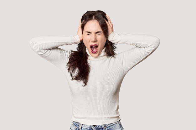 Mujer caucásica joven en un estudio cubriendo los oídos con las manos tratando de no oír un sonido demasiado fuerte