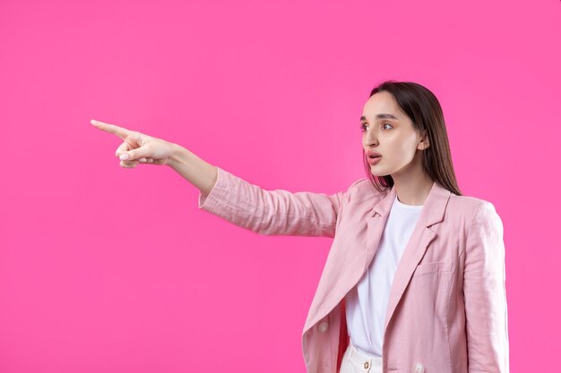 Mujer caucásica joven feliz en una chaqueta rosa que señala con el dedo