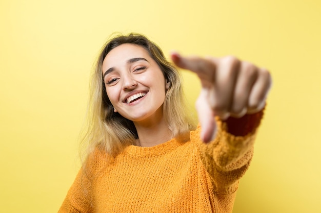 Mujer caucásica joven feliz en un suéter naranja señalando con el dedo mostrando espacio de copia para su texto