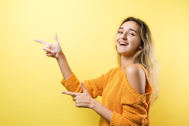 Mujer caucásica joven feliz en un suéter naranja señalando con el dedo mostrando espacio de copia para su texto