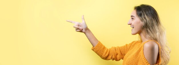 Mujer caucásica joven feliz en un suéter naranja señalando con el dedo