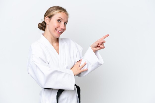 Mujer caucásica joven haciendo karate aislado sobre fondo blanco apuntando con el dedo al lado