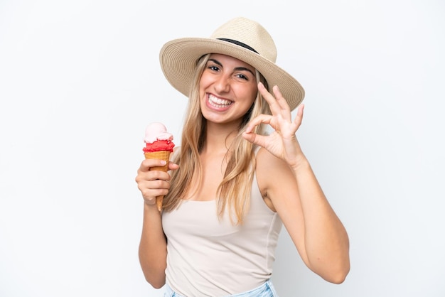 Mujer caucásica joven con un helado de cucurucho aislado sobre fondo blanco que muestra el signo de ok con los dedos