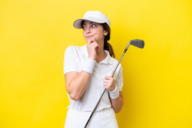 Mujer caucásica joven jugando al golf aislado sobre fondo amarillo y mirando hacia arriba