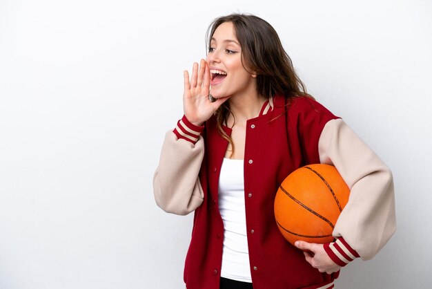 Mujer caucásica joven jugando baloncesto aislado sobre fondo blanco gritando con la boca abierta a un lado