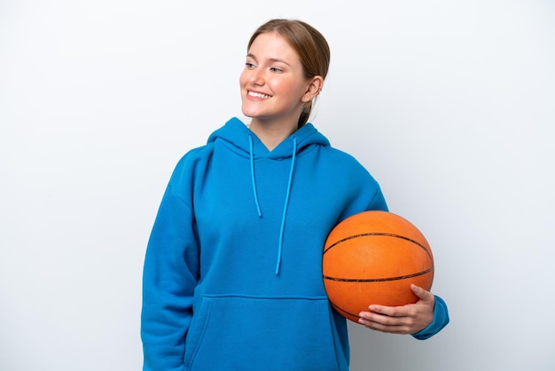 Mujer caucásica joven jugando baloncesto aislado sobre fondo blanco mirando hacia el lado y sonriendo