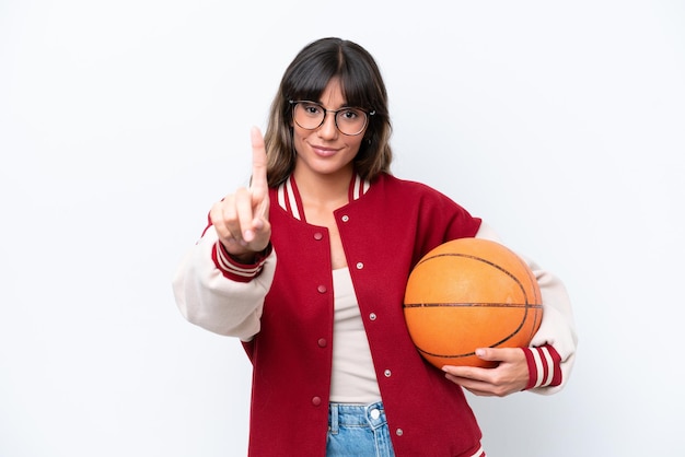 Mujer caucásica joven jugando baloncesto aislado sobre fondo blanco mostrando y levantando un dedo