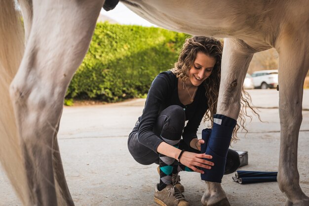 Mujer caucásica joven limpiando y preparando un caballo.