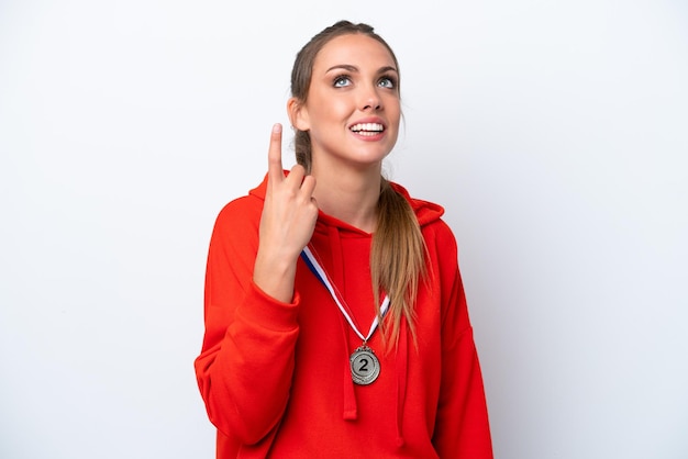 Mujer caucásica joven con medallas aisladas sobre fondo blanco apuntando hacia arriba y sorprendida