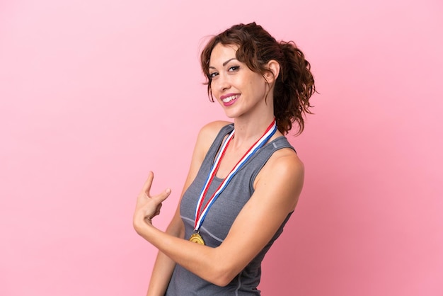 Mujer caucásica joven con medallas aisladas sobre fondo rosa apuntando hacia atrás