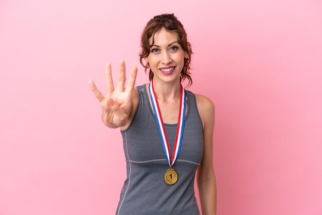 Foto mujer caucásica joven con medallas aisladas sobre fondo rosa feliz y contando cuatro con los dedos