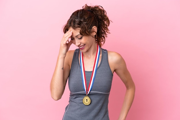 Mujer caucásica joven con medallas aisladas sobre fondo rosa riendo