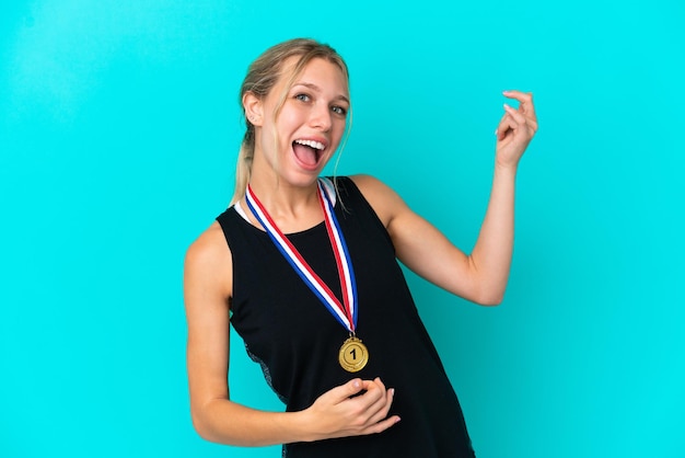 Mujer caucásica joven con medallas aislado sobre fondo azul haciendo gesto de guitarra