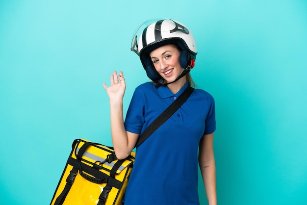 Mujer caucásica joven con mochila térmica aislada sobre fondo blanco saludando con la mano con expresión feliz