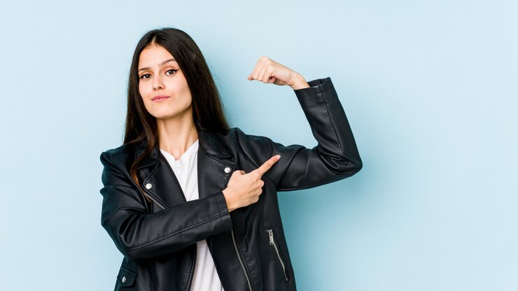 Foto mujer caucásica joven en la pared azul que muestra gesto de fuerza con los brazos