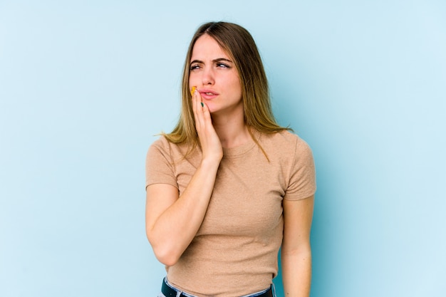 Mujer caucásica joven en la pared azul que tiene un dolor de dientes fuerte, dolor molar.