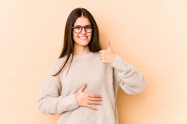 La mujer caucásica joven en la pared beige toca la panza, sonríe suavemente