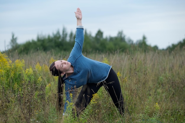 Mujer caucásica joven practica yoga en el parque de hierba verde