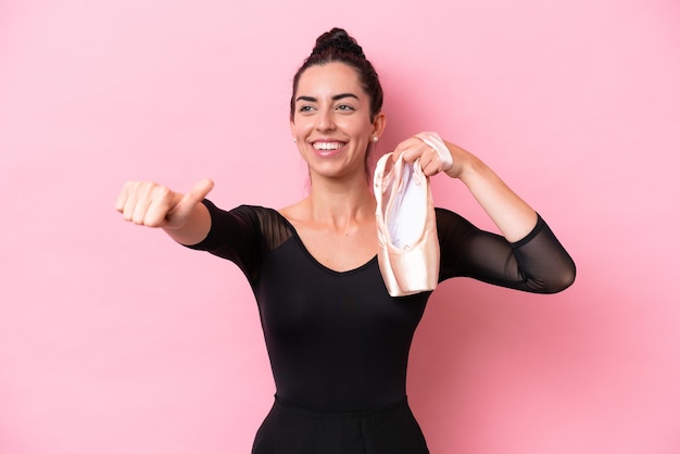 Mujer caucásica joven practicando ballet aislado sobre fondo rosa dando un gesto de aprobación