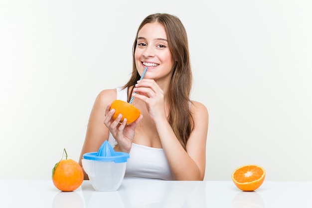 Mujer caucásica joven que bebe una naranja con una paja.