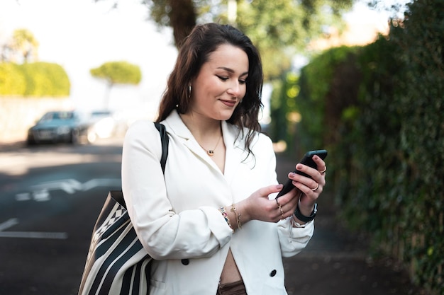 Mujer caucásica joven que camina en la calle usando un teléfono inteligente