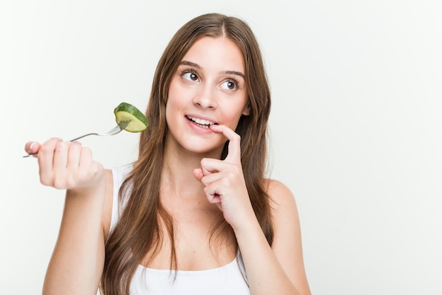 La mujer caucásica joven que come el pepino se relajó pensando en algo que mira un espacio en blanco.