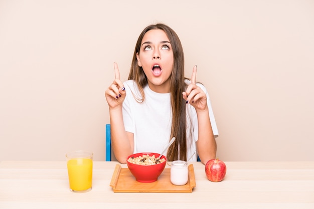 Mujer caucásica joven que desayuna apuntando al revés con la boca abierta.