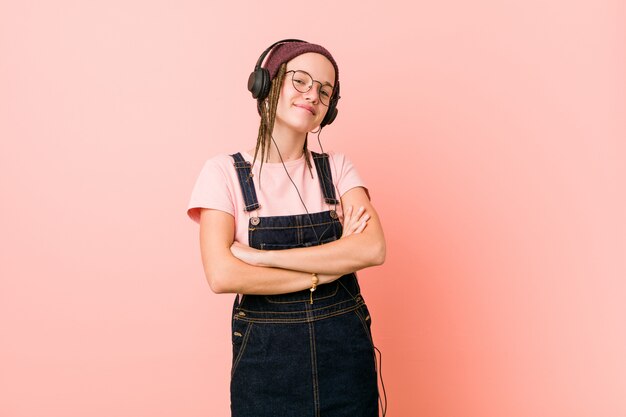 Mujer caucásica joven que escucha la música que sonríe confiada con los brazos cruzados.