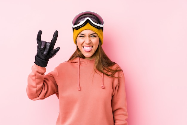 Mujer caucásica joven que lleva una ropa del esquí aislada mostrando un gesto de los cuernos como concepto de la revolución.