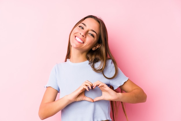 La mujer caucásica joven que llevaba un esquí viste aislado sonriendo y mostrando una forma del corazón con las manos.