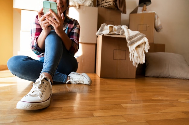 Mujer caucásica joven que mira el teléfono móvil delante de la pila de cajas de cartón Espacio de copia