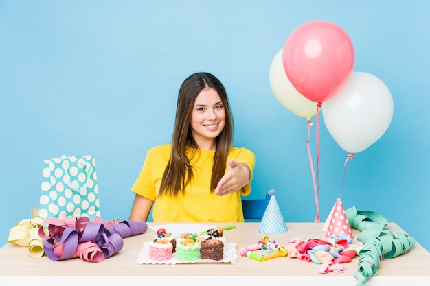 Mujer caucásica joven que organiza un cumpleaños que estira la mano en gesto de saludo.