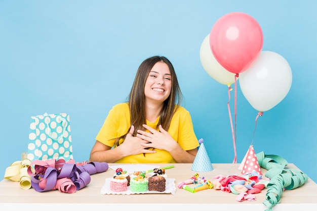 Mujer caucásica joven que organiza un cumpleaños se ríe felizmente y se divierte manteniendo las manos en el estómago.