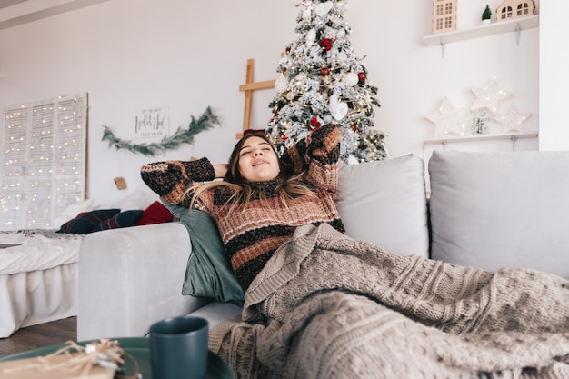 Mujer caucásica joven que se relaja en un sofá en casa en las vacaciones de Navidad.