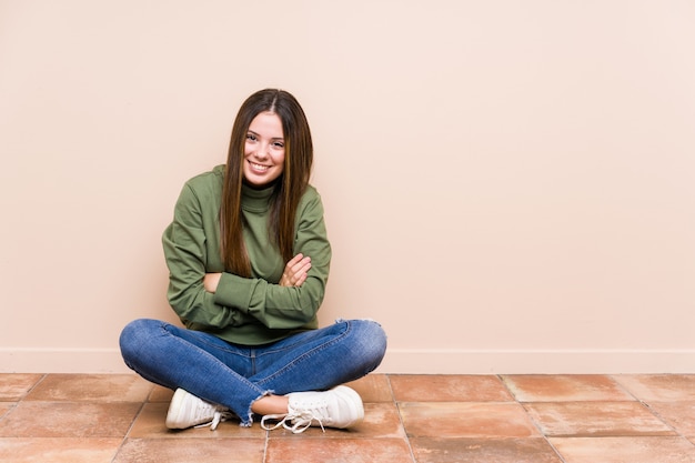 La mujer caucásica joven que se sentaba en el piso aisló reír y divertirse.