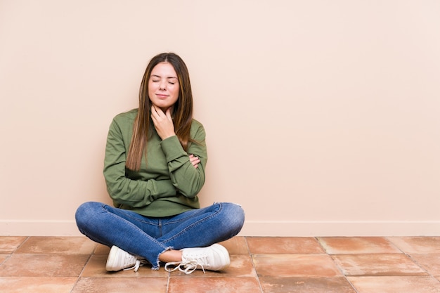 La mujer caucásica joven que se sienta en el piso aislada sufre dolor en la garganta debido a un virus o infección.