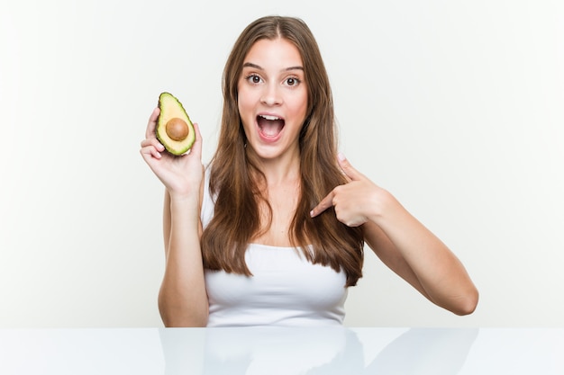 La mujer caucásica joven que sostenía un aguacate sorprendió señalar él mismo, sonriendo ampliamente.