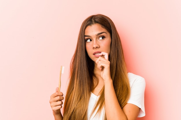 La mujer caucásica joven que sostenía un cepillo de dientes relajado pensando en algo que miraba un espacio en blanco.