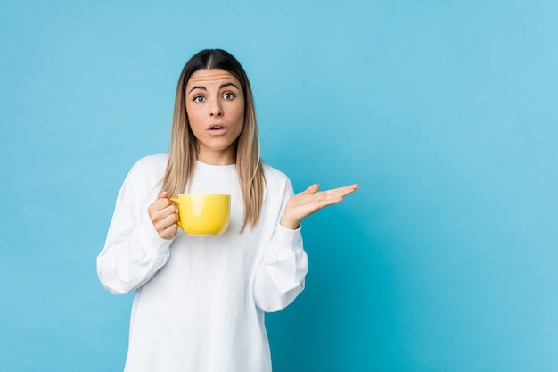 La mujer caucásica joven que sostenía una taza de café impresionó llevar a cabo el espacio de la copia en la palma.