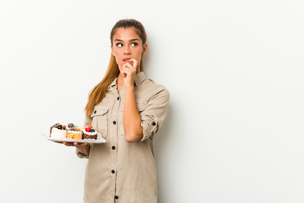 La mujer caucásica joven que sostenía las tortas dulces se relajó pensando en algo que miraba un espacio de la copia.