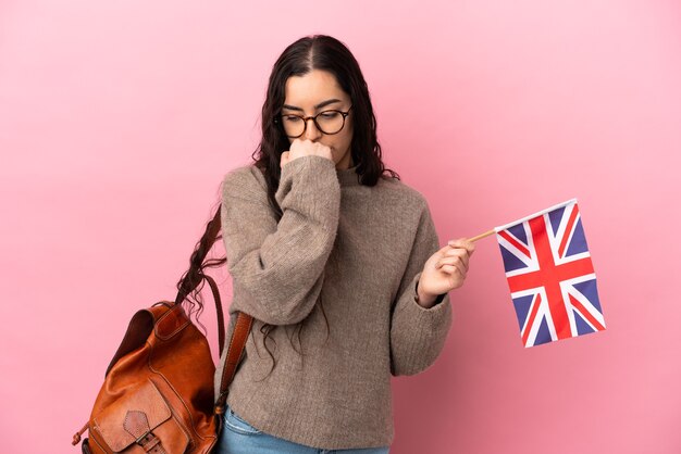 Mujer caucásica joven que sostiene una bandera del Reino Unido aislada en la pared rosada que tiene dudas